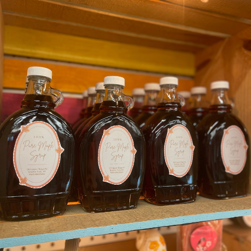 Glass jars of maple. syrup posed on a shelf.